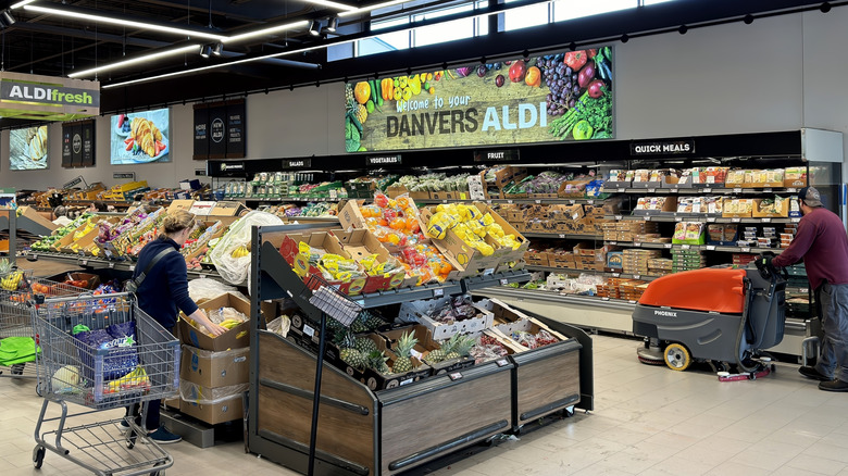 Interior of Aldi produce section with shoppers and floor cleaner.