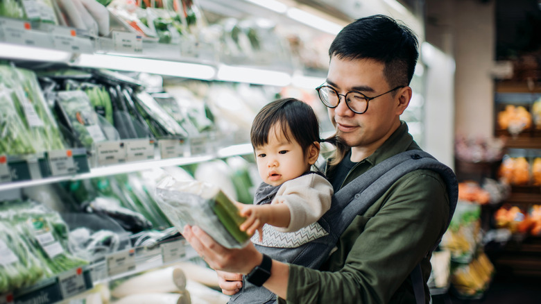 Father and young child in carrier shopping in produce section.