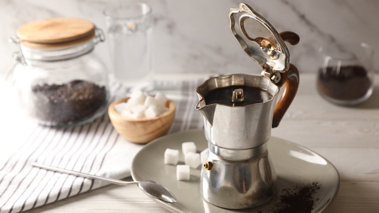 Moka pot on a plate with sugar cubes and a spoon