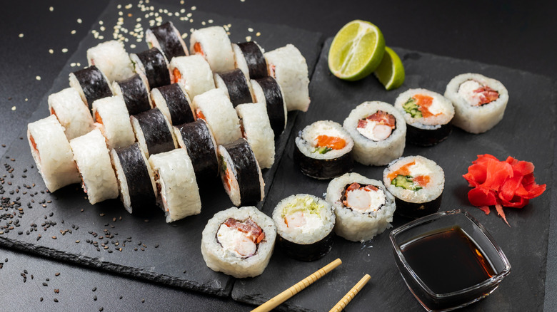 a plate of sushi rolls served with sesame seeds, lime, and soy sauce