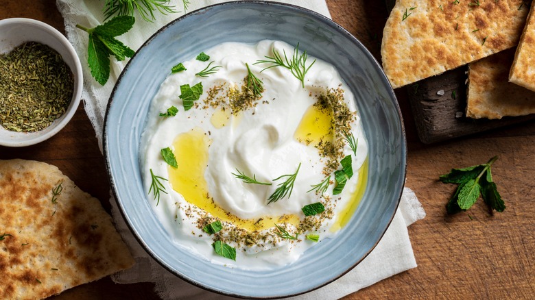 Labneh in a bowl with herbs, olive oil, and bread