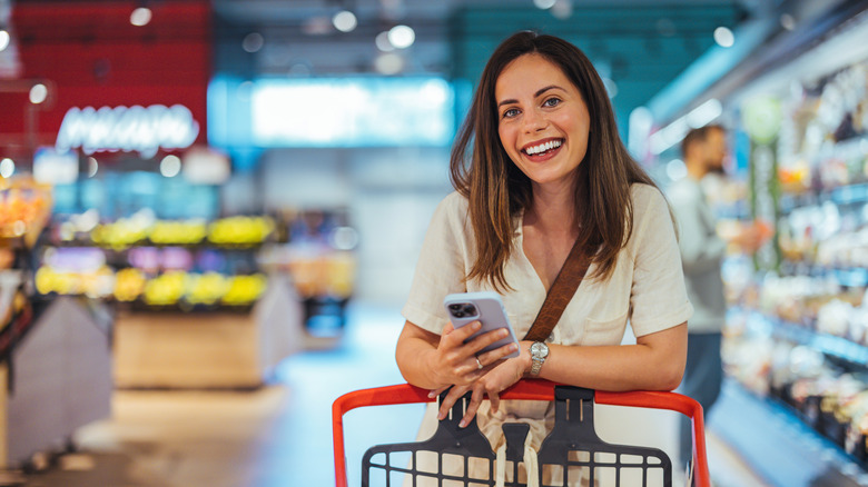 A woman smiling while standing at grocery cart in store.