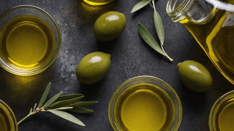 Glass cups of olive oil, olives scattered around