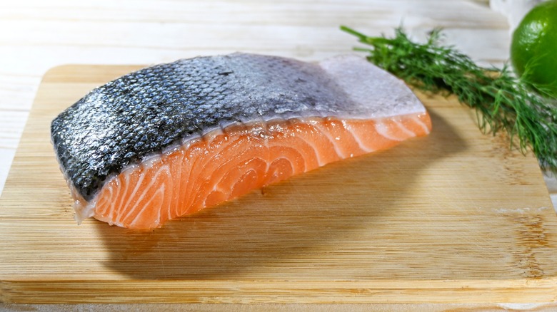 Raw salmon filet with skin on wood cutting board