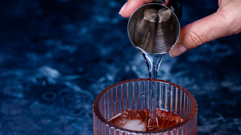 Person pouring water from a shot glass to a glass