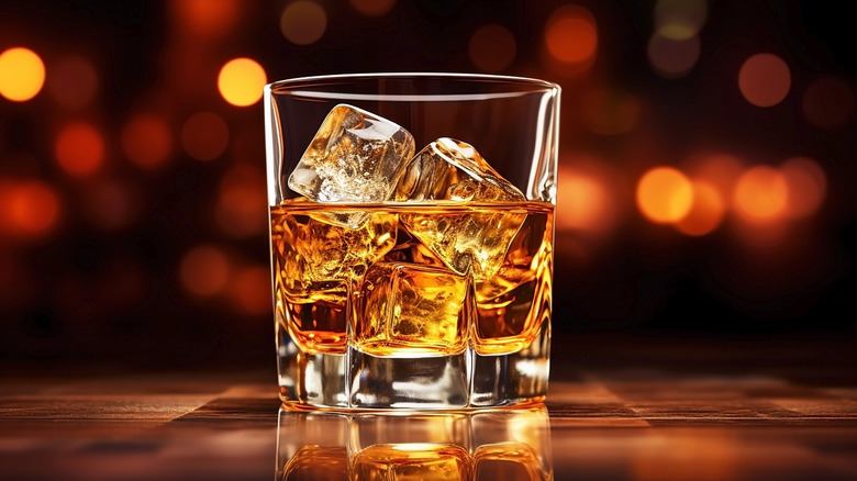 Whiskey with ice cubes in glass on background of lights.