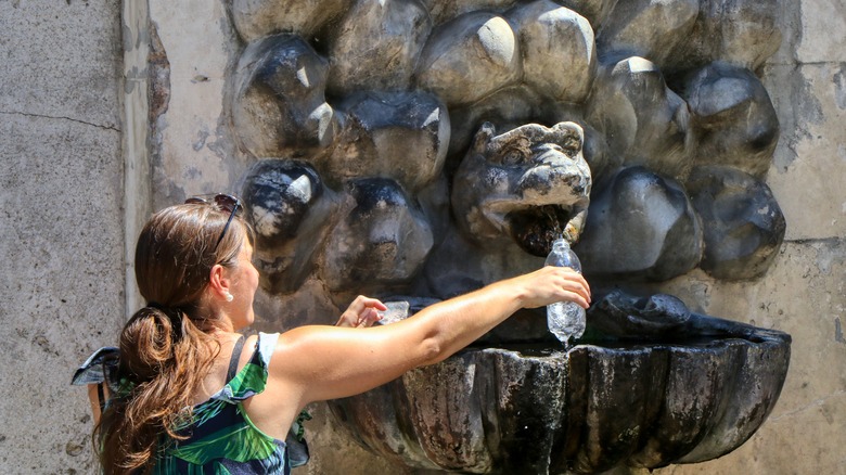 Woman filling a water bottle from a historic fountain