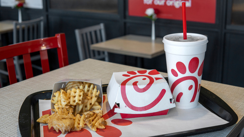 Chick-fil-A sandwich, waffle fries, and drink on black tray on table.