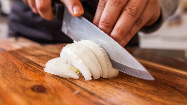 Person slicing onion with knife on wood board