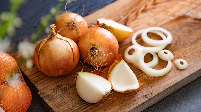 Whole onions and slices on wooden cutting board.