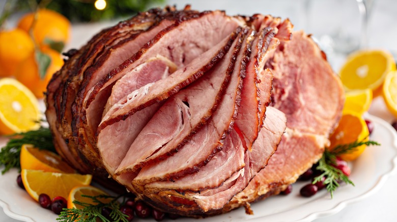 Spiral cut ham on white plate with oranges and cranberries.