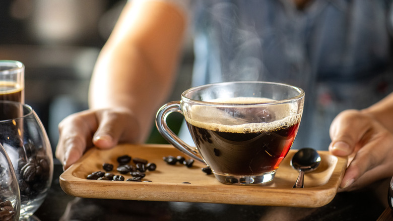 Black drip coffee being served in a glass cup.