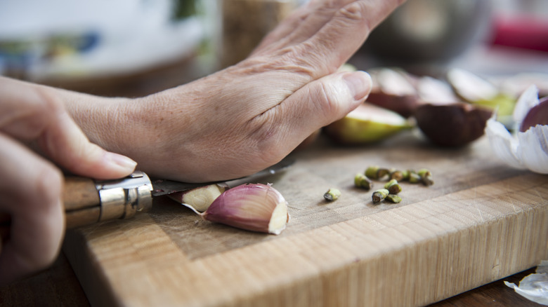 Woman using a knife and her hands to peel fresh garlic cloves on a wooden cutting board..