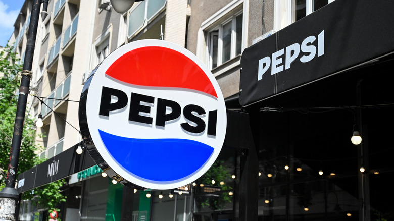 Round Pepsi sign hanging above sidewalk.