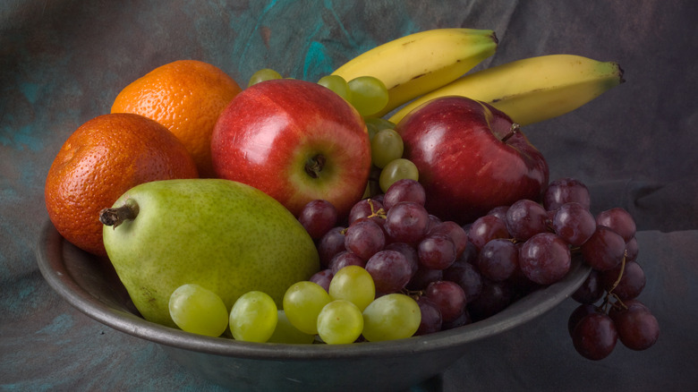 Fruit bowl with grapes, apples, oranges, bananas, and a pear