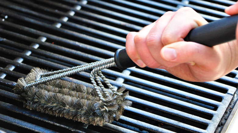 Man's hand using grill a brush on a grate