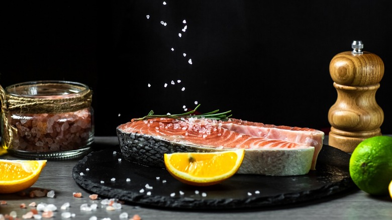 Salt sprinkled onto fish with citrus fruits around