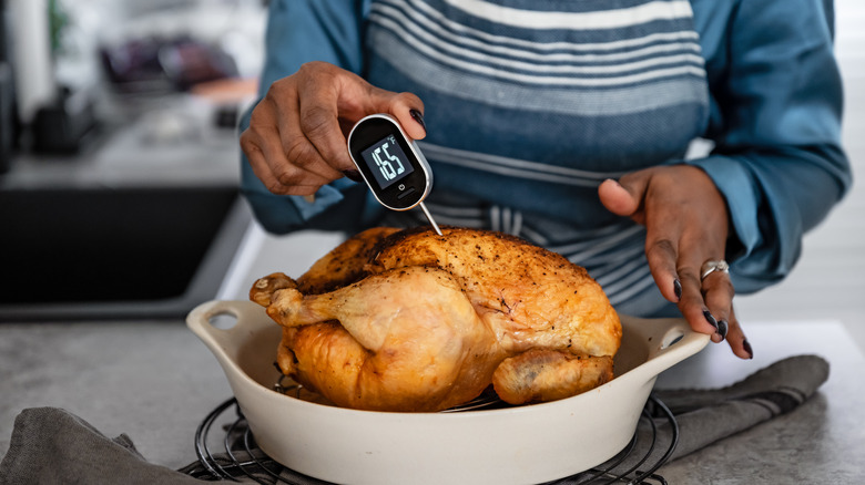 woman using a meat thermometer to test a cooked chicken; the thermometer reads 165 degrees