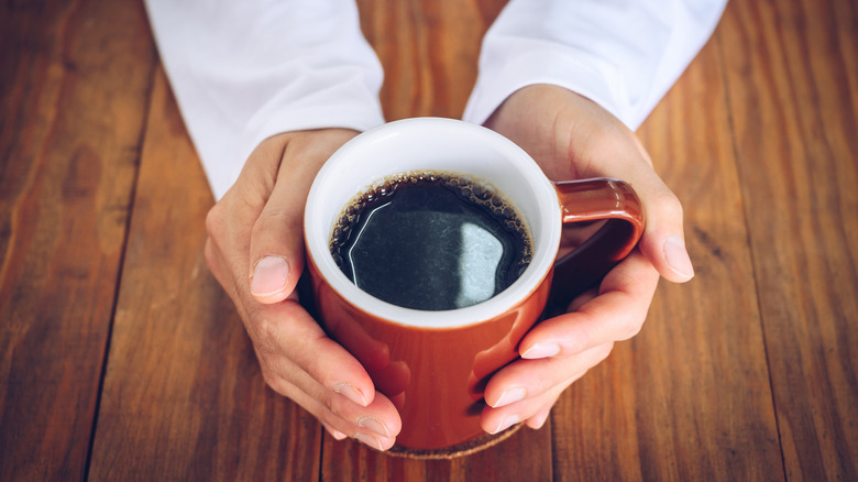 Two hands cradle a mug of coffee