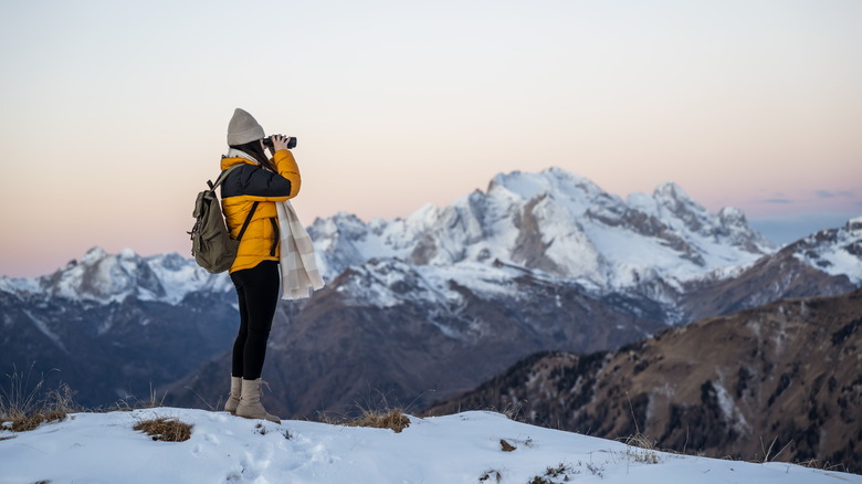 woman standing on a snowy mountain and looking through binoculars