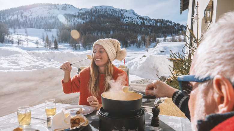woman eating fondue outdoors with snowy mountains in the background