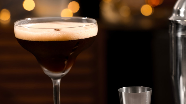 Chocolate martini next to a shaker and jigger, dark background with subtle lighting.