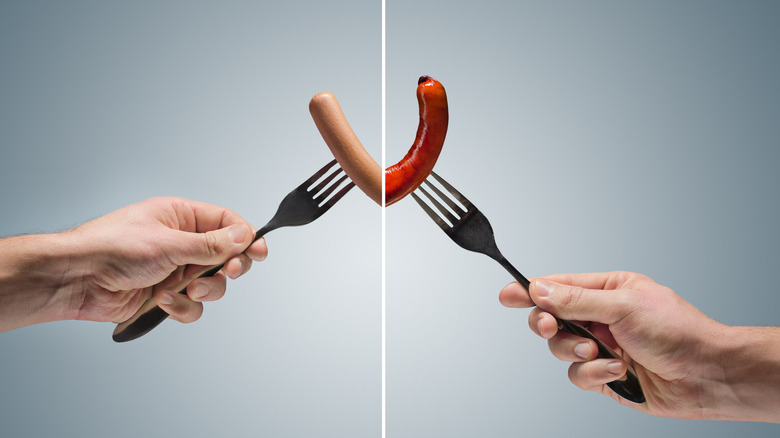 Two hands holding forks with hot dogs