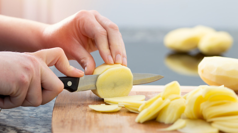slicing up peeled potato on cutting board