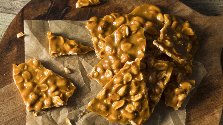 Peanut brittle on a cutting board with crumpled wax paper.